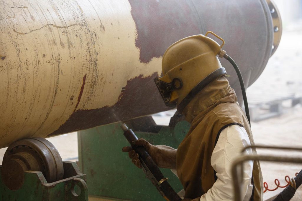 A welder performing metal surface preparation on a large pipe.